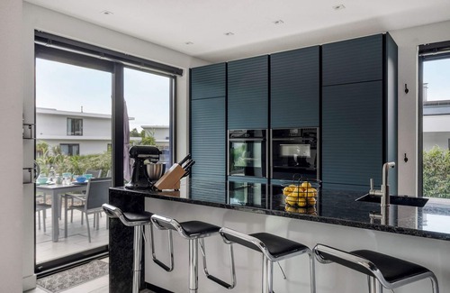 Zeewolde House | Detached 6-person villa by the water with a cosy living room featuring a piano and fireplace, modern kitchen with cooking island, and a sunny garden with lounge set.
