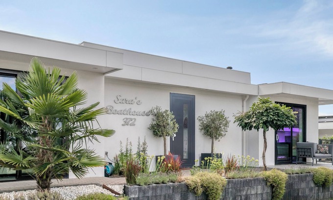 Zeewolde House | Detached 6-person villa by the water with a cosy living room featuring a piano and fireplace, modern kitchen with cooking island, and a sunny garden with lounge set.